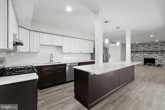 kitchen with pendant lighting, white cabinetry, stainless steel appliances, sink, and a brick fireplace