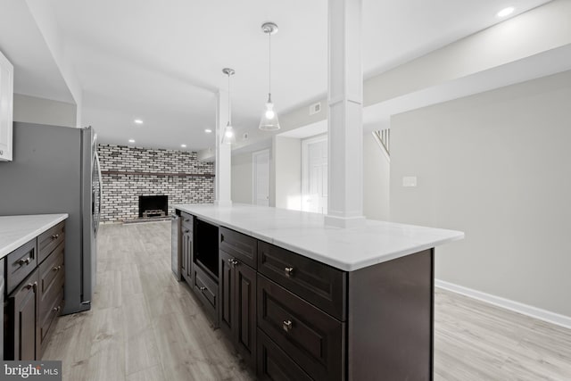 kitchen with decorative light fixtures, a center island, a brick fireplace, and light wood-type flooring