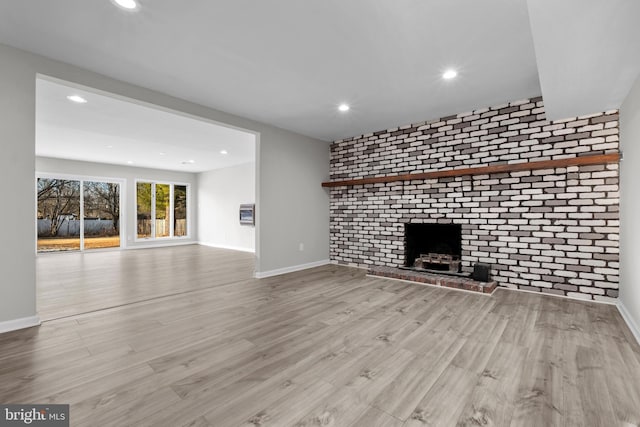 unfurnished living room featuring light wood-type flooring, a brick fireplace, and brick wall