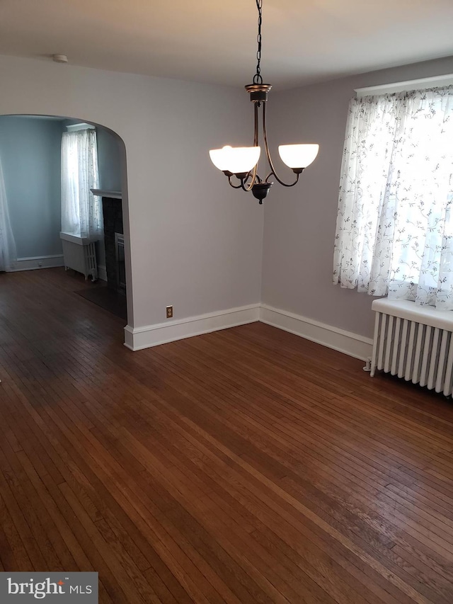 unfurnished room with dark wood-type flooring, radiator, a notable chandelier, and plenty of natural light