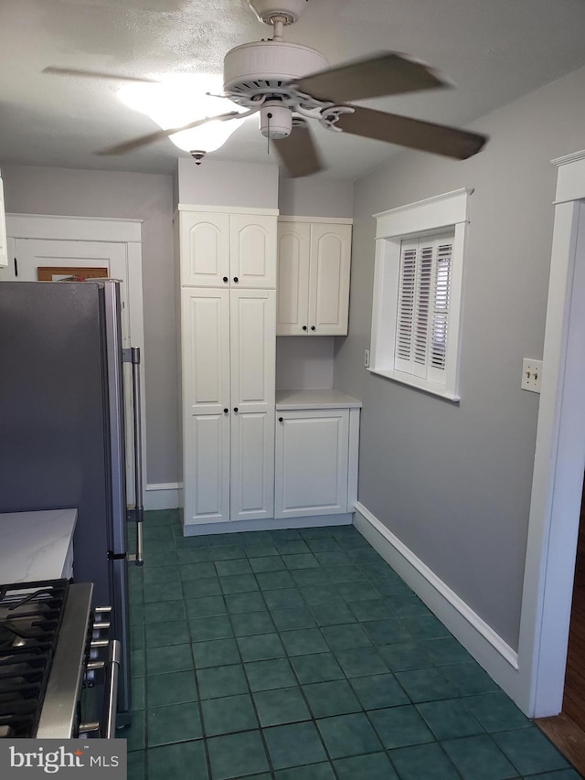 kitchen with ceiling fan, dark tile patterned flooring, white cabinets, and stainless steel refrigerator