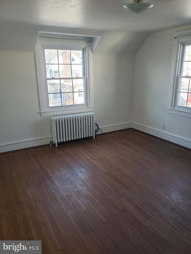 additional living space with radiator, a healthy amount of sunlight, lofted ceiling, and dark hardwood / wood-style floors