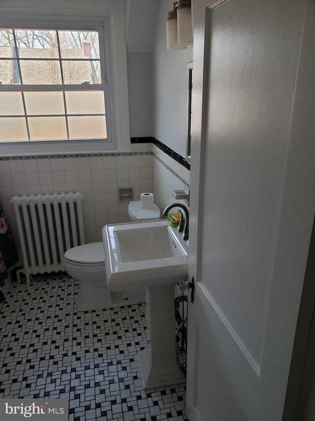 bathroom with toilet, sink, tile walls, and radiator heating unit