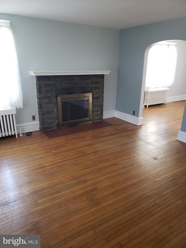 unfurnished living room featuring radiator, dark hardwood / wood-style flooring, and a stone fireplace