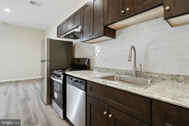 kitchen featuring stainless steel appliances, decorative backsplash, light wood-type flooring, light stone countertops, and sink