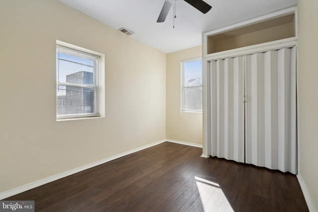 unfurnished bedroom featuring ceiling fan, dark hardwood / wood-style flooring, a closet, and multiple windows