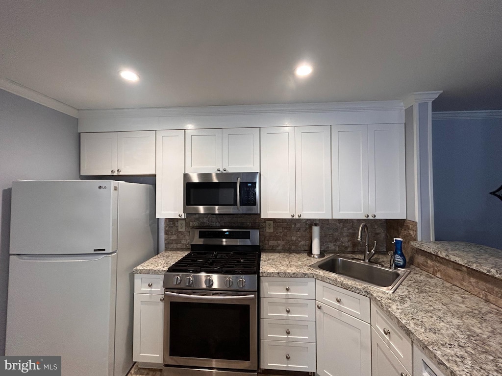 kitchen featuring appliances with stainless steel finishes, backsplash, ornamental molding, white cabinets, and sink