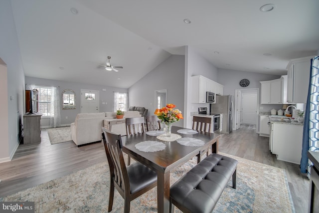 dining area with ceiling fan, high vaulted ceiling, sink, and light wood-type flooring