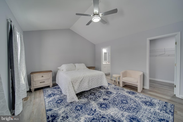 bedroom featuring ceiling fan, vaulted ceiling, connected bathroom, a walk in closet, and light wood-type flooring