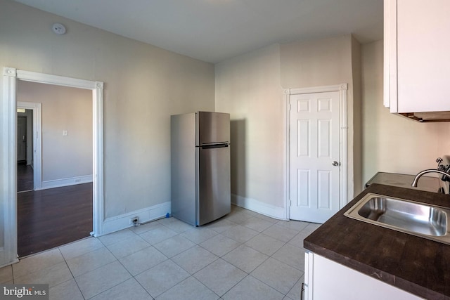 kitchen with light tile patterned flooring, sink, white cabinets, and stainless steel refrigerator