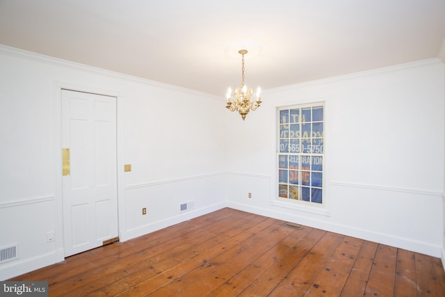 spare room with wood-type flooring, ornamental molding, and an inviting chandelier