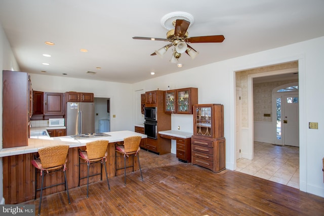 kitchen featuring ceiling fan, a kitchen bar, kitchen peninsula, black microwave, and stainless steel fridge