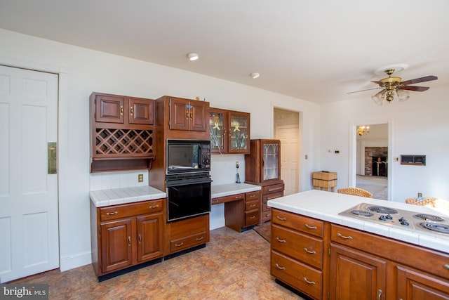 kitchen featuring ceiling fan, tile countertops, a brick fireplace, and black appliances