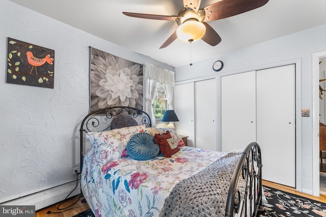 bedroom with ceiling fan, wood-type flooring, a baseboard heating unit, and multiple closets