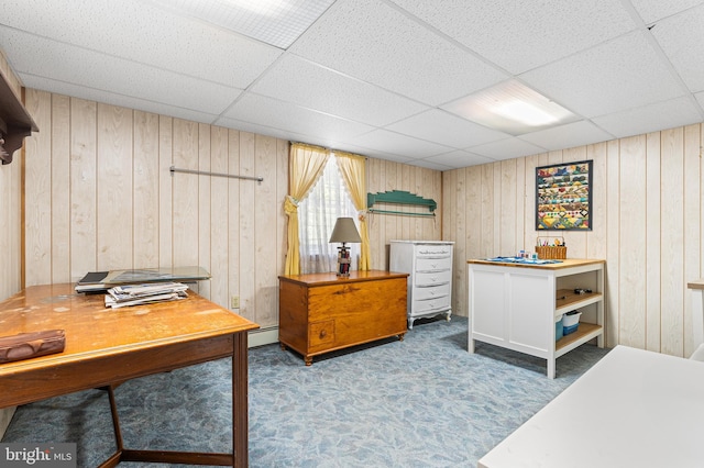 carpeted bedroom featuring wood walls, baseboard heating, and a drop ceiling