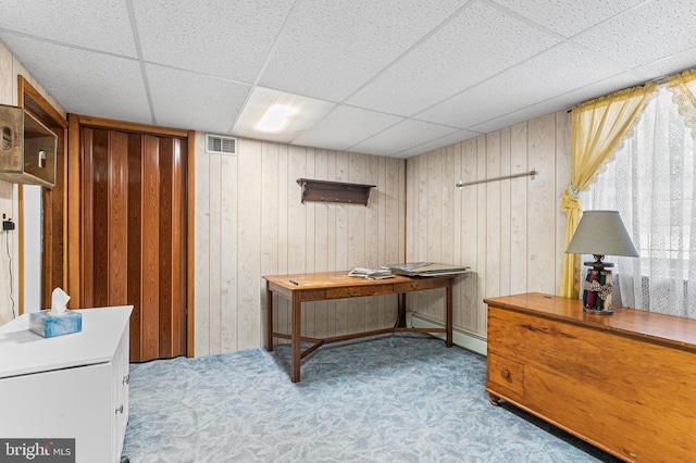 interior space featuring a paneled ceiling, wood walls, and a baseboard radiator