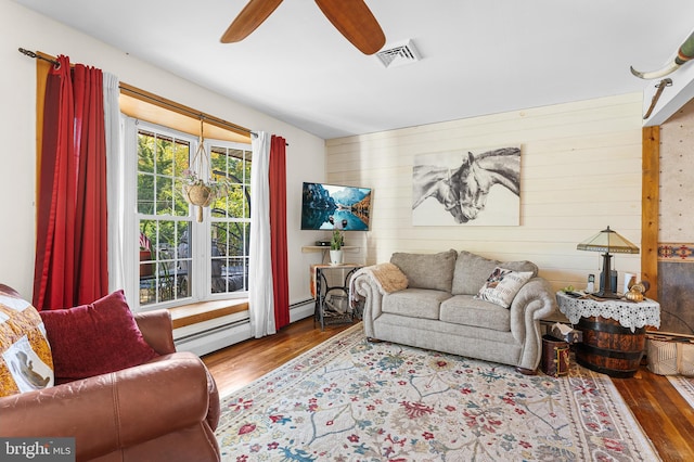 living room with ceiling fan, baseboard heating, wood walls, and hardwood / wood-style floors