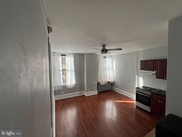 kitchen featuring ceiling fan, stove, sink, radiator, and dark hardwood / wood-style flooring