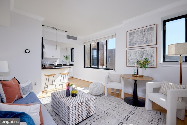 living room featuring baseboards, light wood-style floors, visible vents, and crown molding