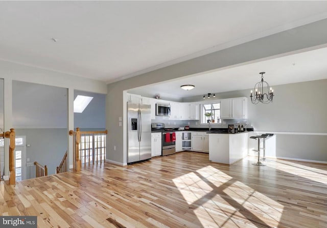 kitchen with kitchen peninsula, appliances with stainless steel finishes, decorative light fixtures, a chandelier, and white cabinets