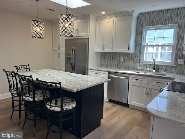 kitchen featuring pendant lighting, a kitchen island, white cabinetry, stainless steel appliances, and sink