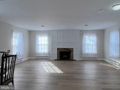 unfurnished living room with dark wood-type flooring, a baseboard heating unit, and a fireplace