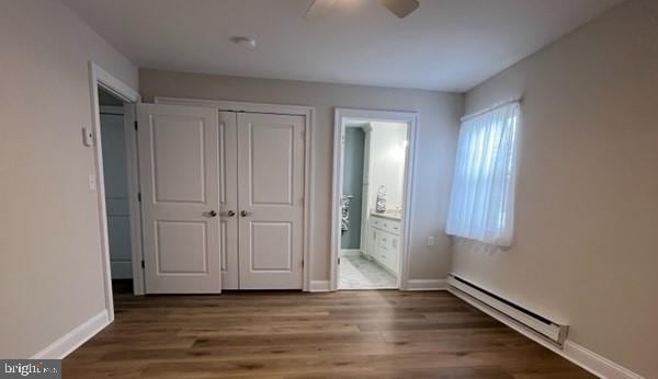 unfurnished bedroom with baseboard heating, ensuite bath, hardwood / wood-style flooring, a closet, and ceiling fan