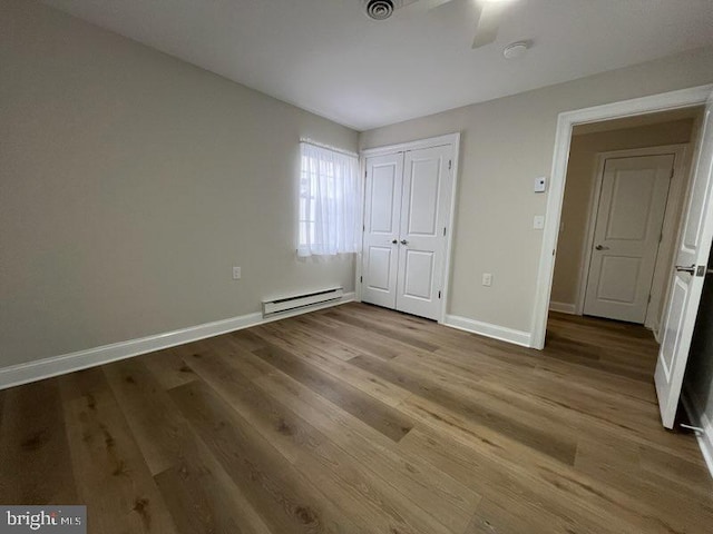 unfurnished bedroom with baseboard heating, a closet, hardwood / wood-style floors, and ceiling fan