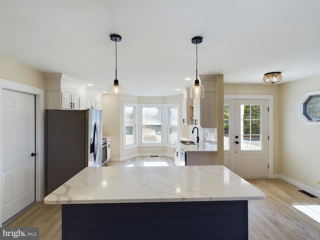 kitchen with sink, white cabinets, light stone counters, and decorative light fixtures