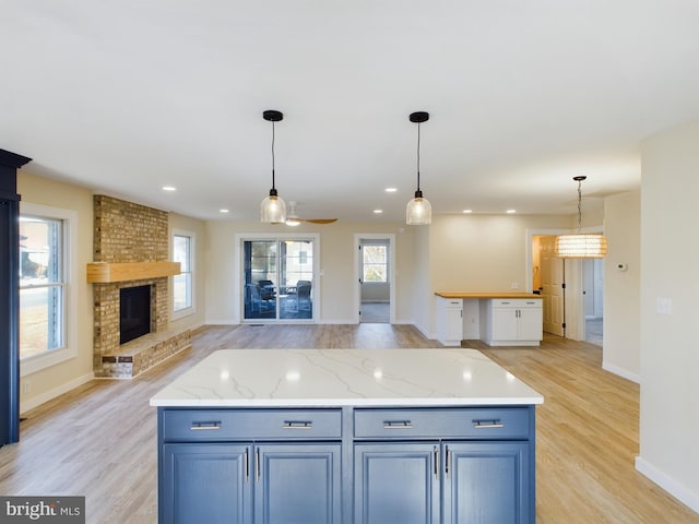 kitchen featuring decorative light fixtures, light hardwood / wood-style floors, a brick fireplace, and a center island