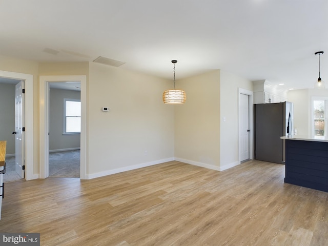 interior space featuring decorative light fixtures, white cabinets, stainless steel refrigerator, and light hardwood / wood-style flooring