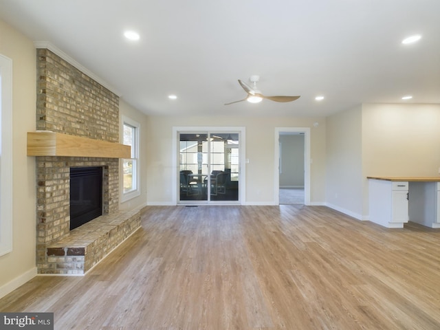 unfurnished living room featuring a brick fireplace, ceiling fan, and light wood-type flooring