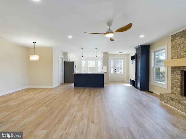 unfurnished living room with light wood-type flooring, a brick fireplace, and ceiling fan