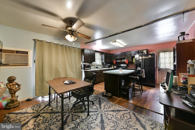 interior space with ceiling fan, appliances with stainless steel finishes, a kitchen breakfast bar, dark hardwood / wood-style flooring, and a kitchen island