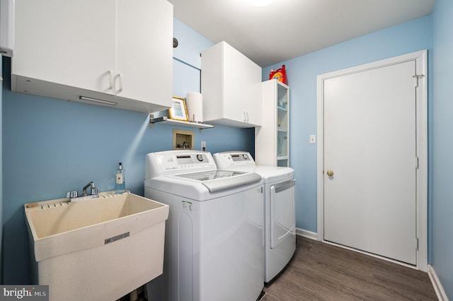 clothes washing area featuring cabinets, sink, washing machine and clothes dryer, and dark hardwood / wood-style flooring