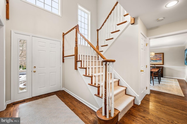 foyer entrance featuring dark hardwood / wood-style flooring, ornamental molding, and a high ceiling