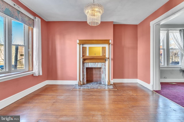 unfurnished living room featuring a high end fireplace, an inviting chandelier, and hardwood / wood-style floors