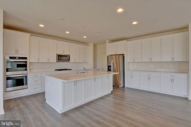 kitchen featuring white cabinetry, stainless steel appliances, light hardwood / wood-style floors, sink, and a kitchen island with sink