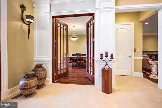 corridor featuring decorative columns, light tile patterned floors, and french doors