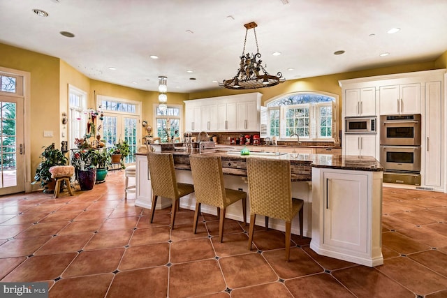 kitchen with a kitchen bar, white cabinetry, a center island, appliances with stainless steel finishes, and dark stone counters