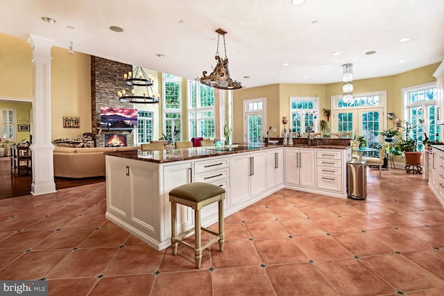 kitchen featuring a kitchen island with sink, hanging light fixtures, white cabinets, and ornate columns