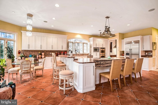 kitchen featuring pendant lighting, white cabinetry, an island with sink, a kitchen bar, and built in appliances