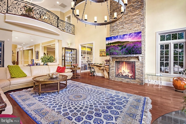 living room with wood-type flooring, a stone fireplace, ornamental molding, and a chandelier