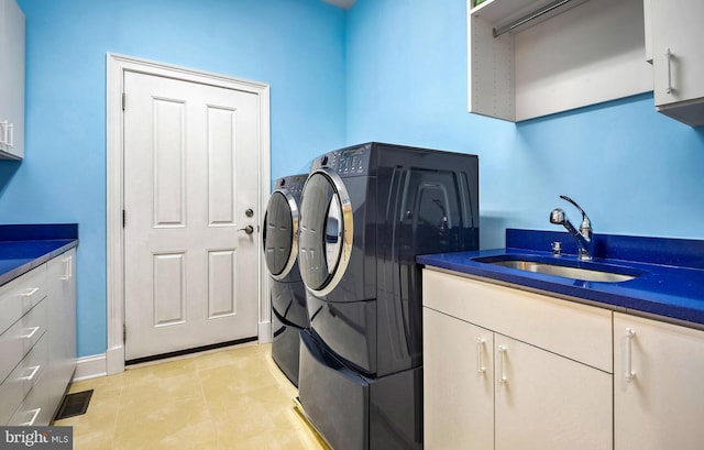 clothes washing area with sink, light tile patterned floors, washing machine and dryer, and cabinets