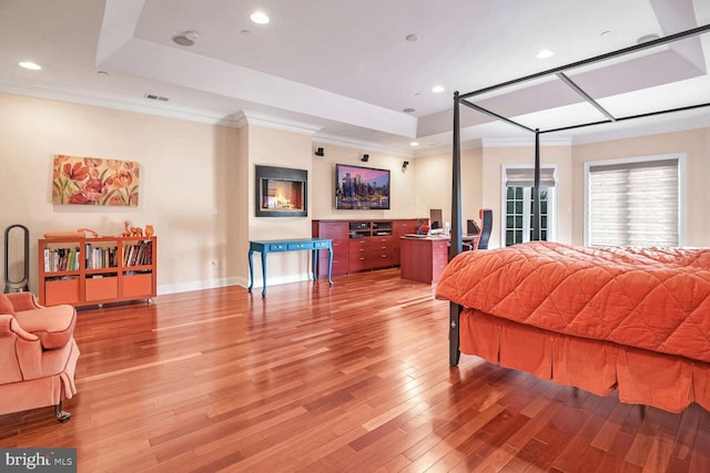 bedroom with crown molding, a tray ceiling, and light hardwood / wood-style flooring