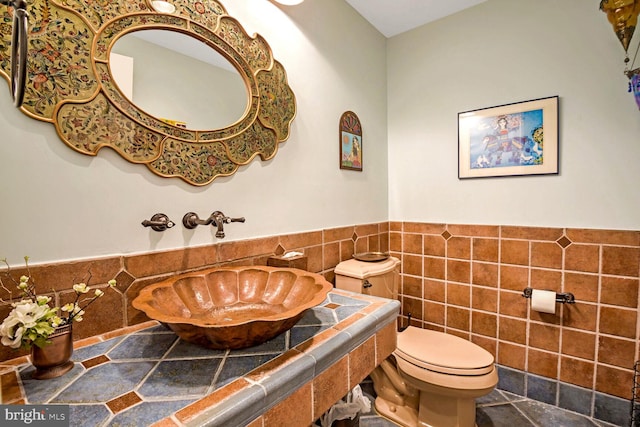 bathroom with toilet, tile patterned flooring, sink, and tile walls