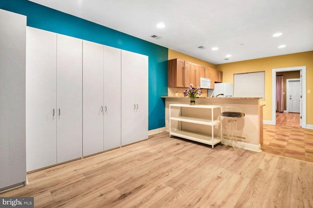 kitchen featuring white appliances, kitchen peninsula, light hardwood / wood-style floors, and a breakfast bar area