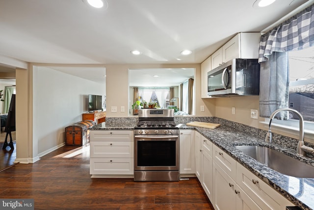 kitchen featuring sink, dark stone countertops, stainless steel appliances, dark hardwood / wood-style floors, and white cabinets