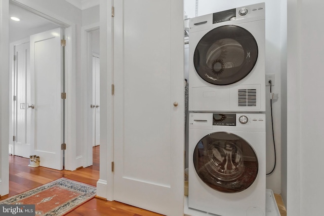 laundry room featuring stacked washer / dryer and wood-type flooring