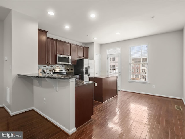 kitchen featuring appliances with stainless steel finishes, dark hardwood / wood-style floors, dark stone counters, a center island, and kitchen peninsula